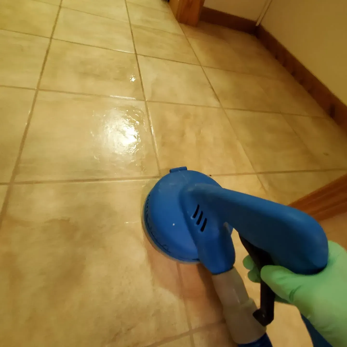 A person is holding a blue spray bottle on a tiled floor.