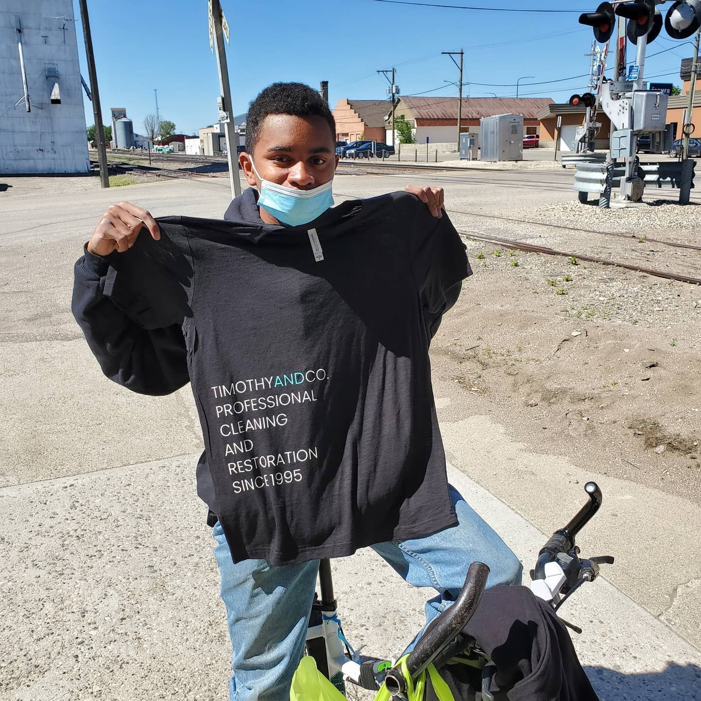 A young boy wearing a mask is holding up a black shirt