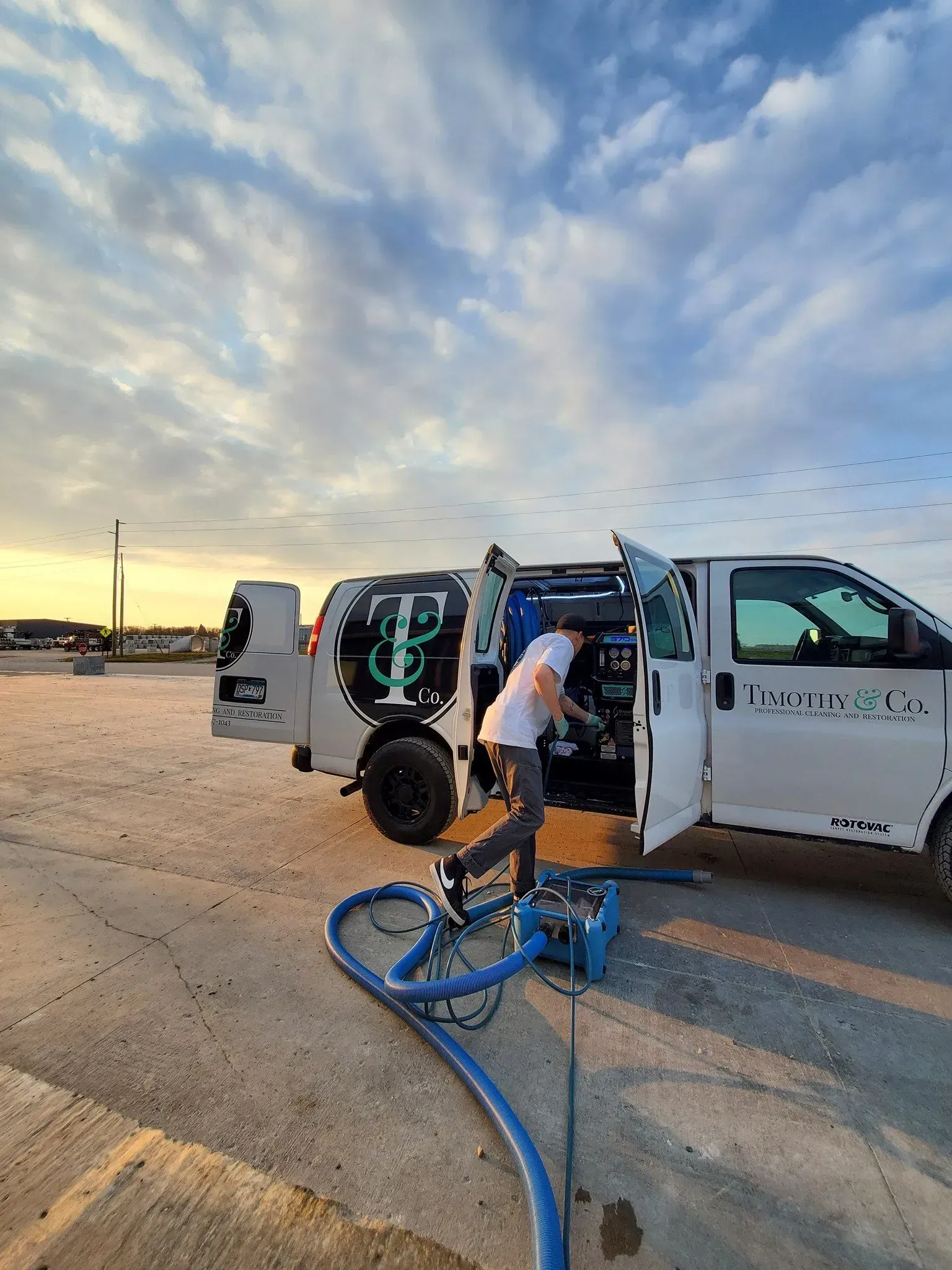 A man is standing in front of a white van with the door open.