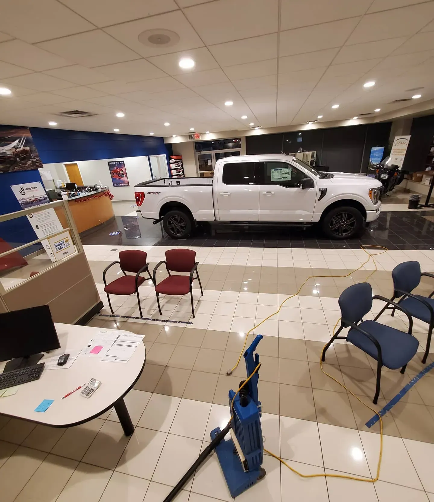 A white truck is parked in a showroom next to a desk and chairs.