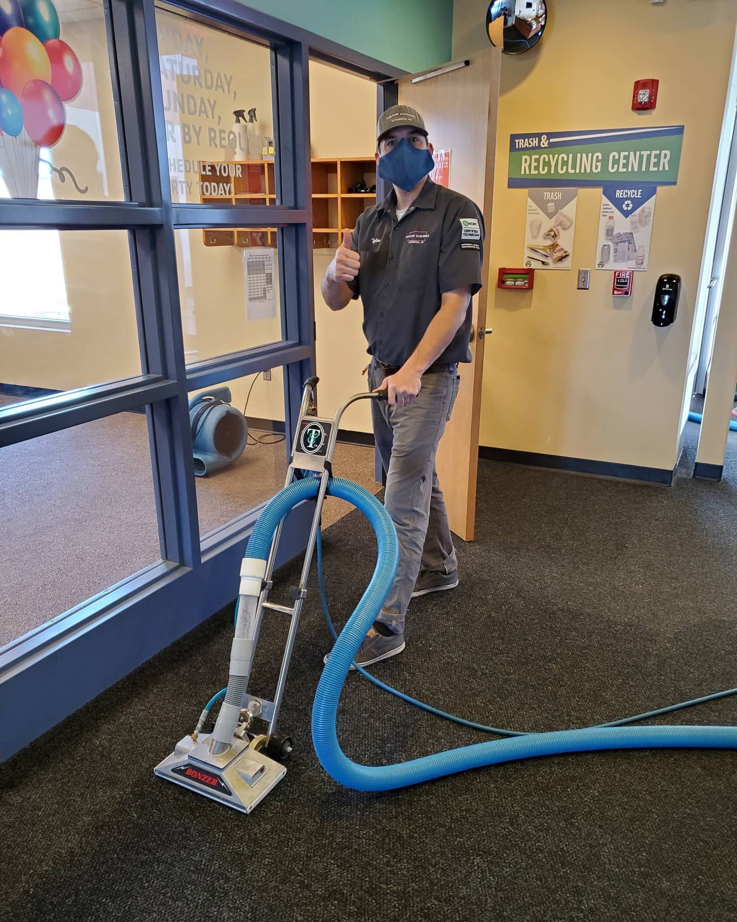 A man wearing a mask is cleaning a carpet with a vacuum cleaner.