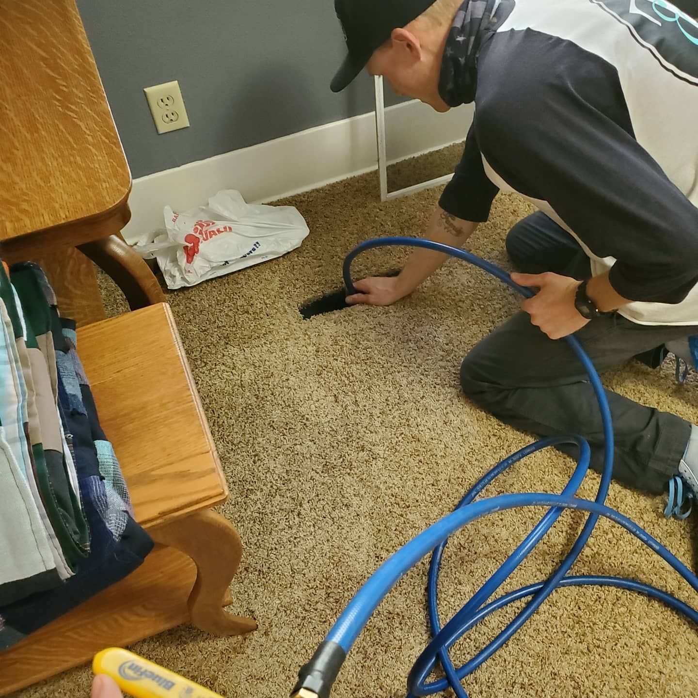 A man is kneeling down on the floor holding a blue hose