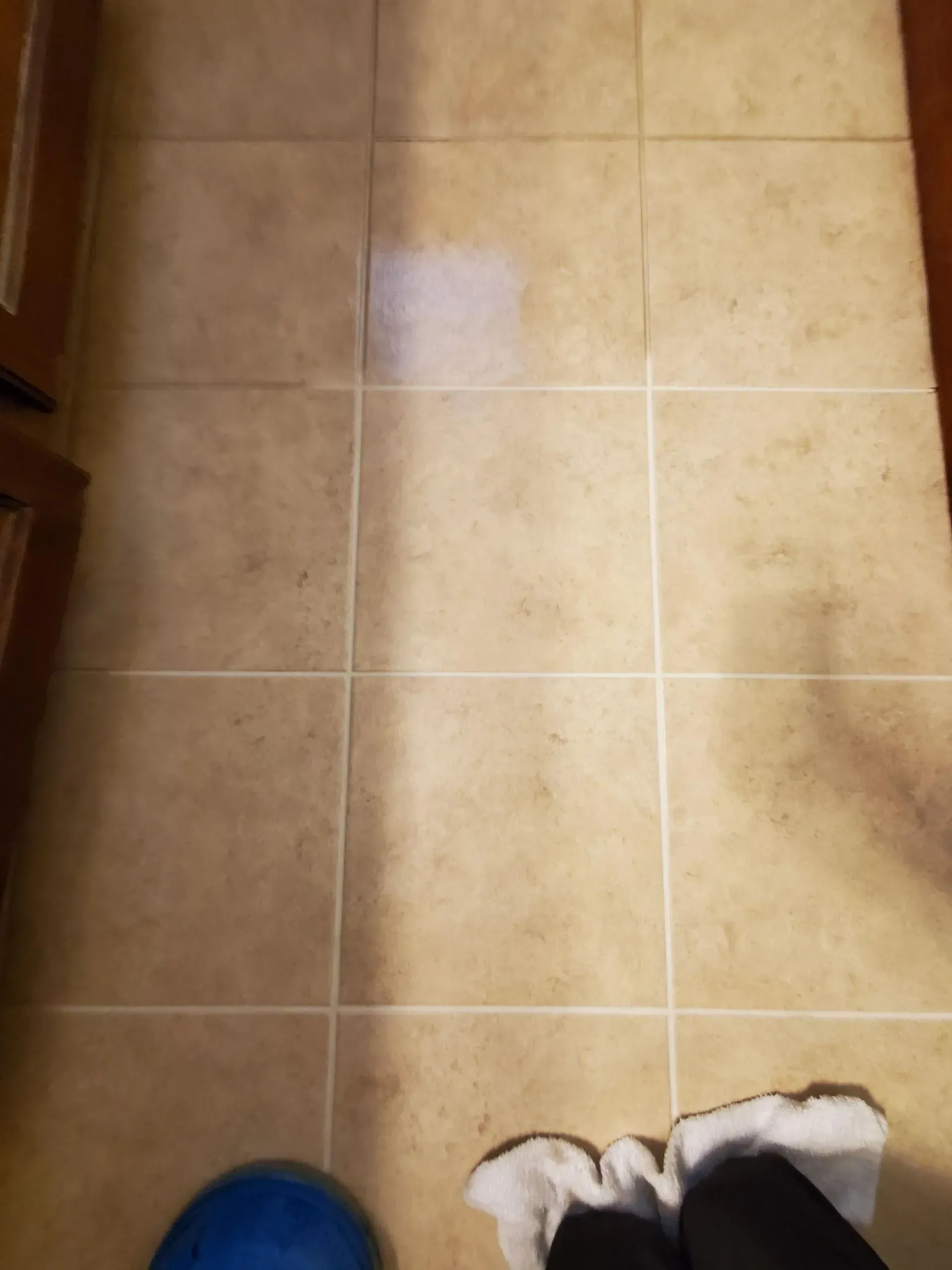 A person is standing on a tiled floor next to a blue ball.