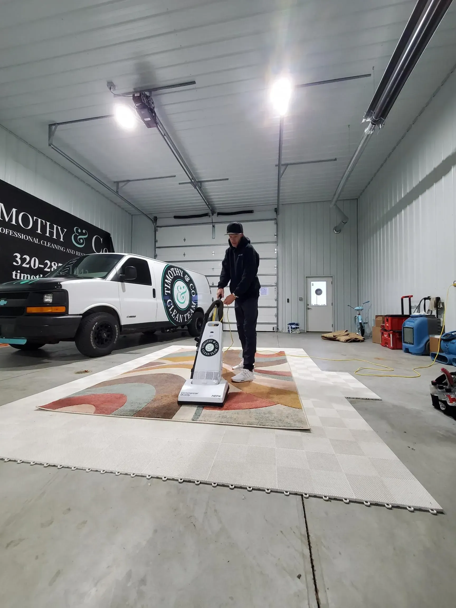 A man is using a vacuum cleaner to clean a rug in a garage.