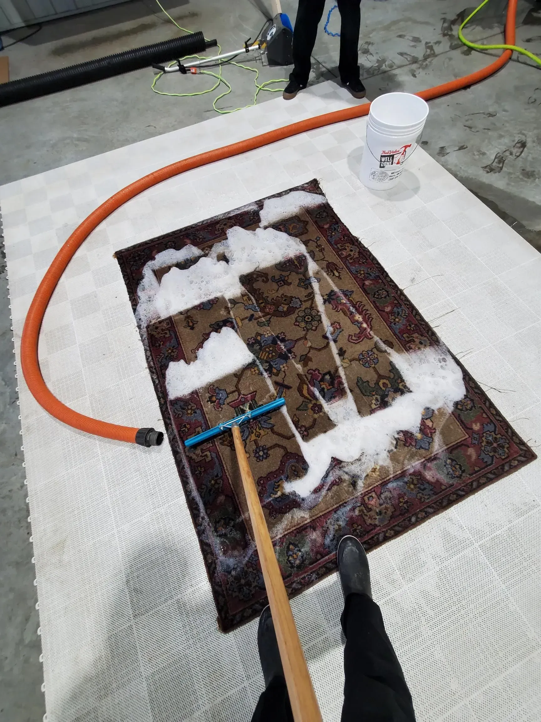 A person is cleaning a rug with a broom.