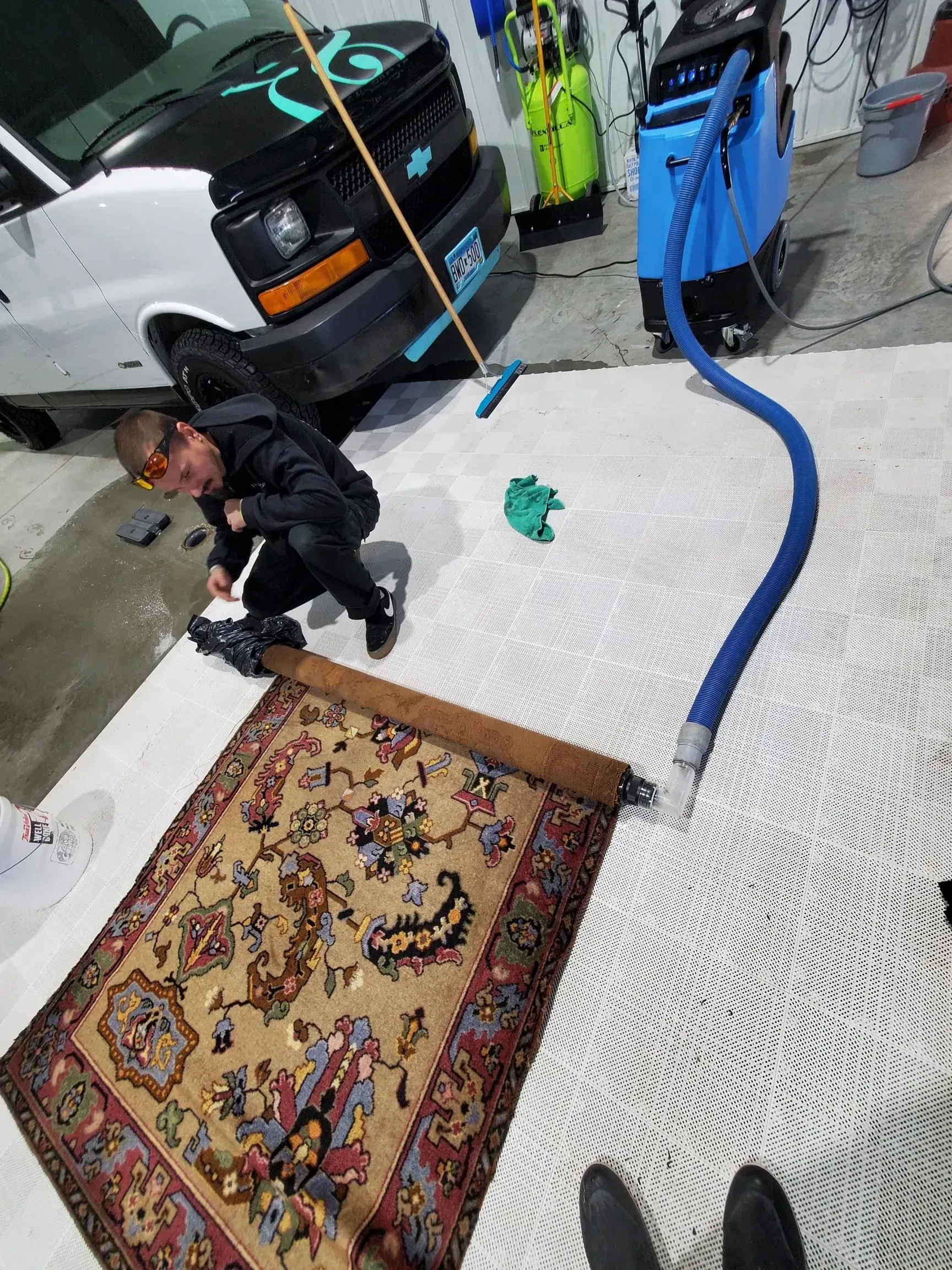 A man is cleaning a rug in a garage with a vacuum cleaner.