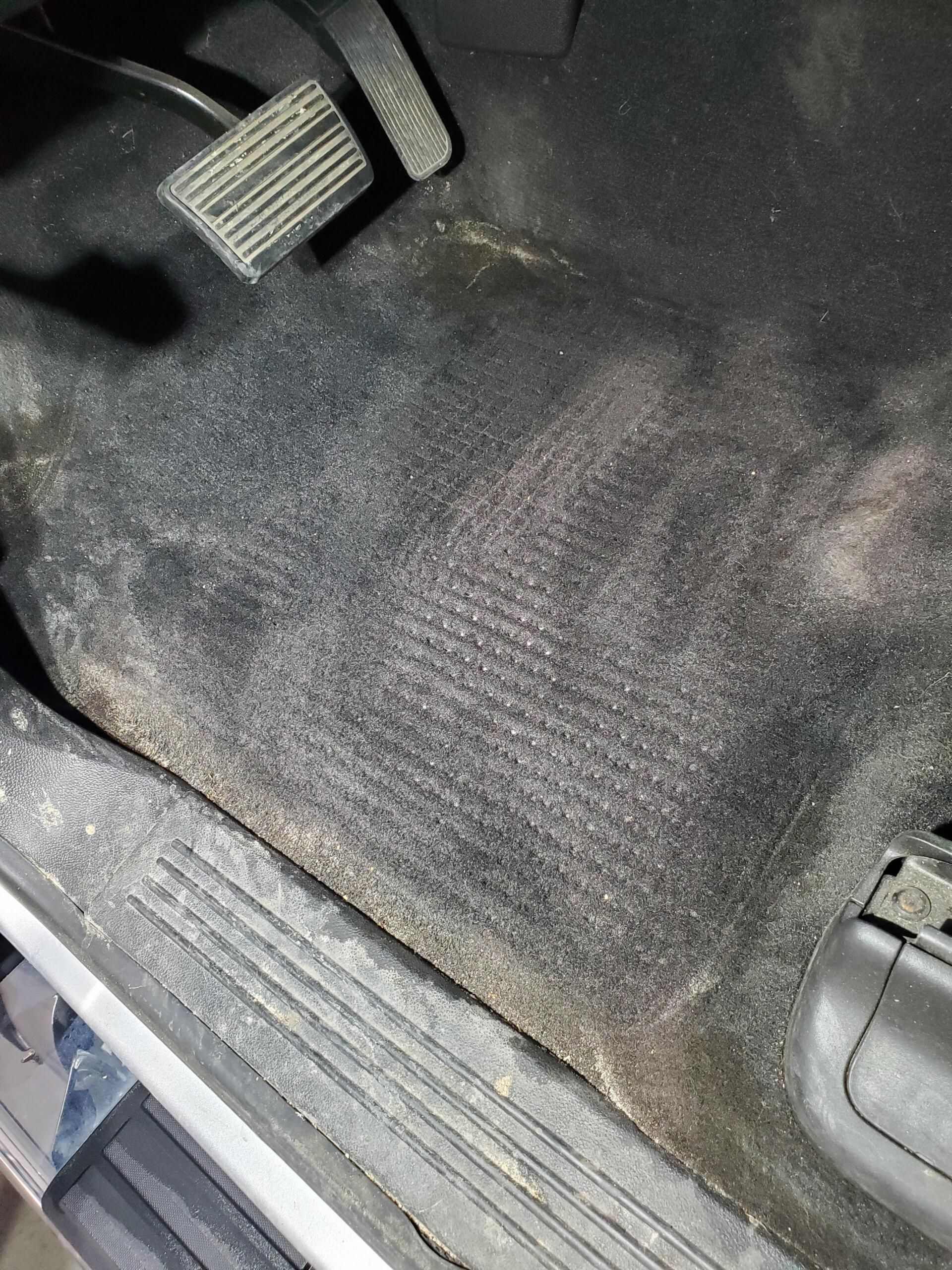 A close up of a dirty car floor with a brake pedal.