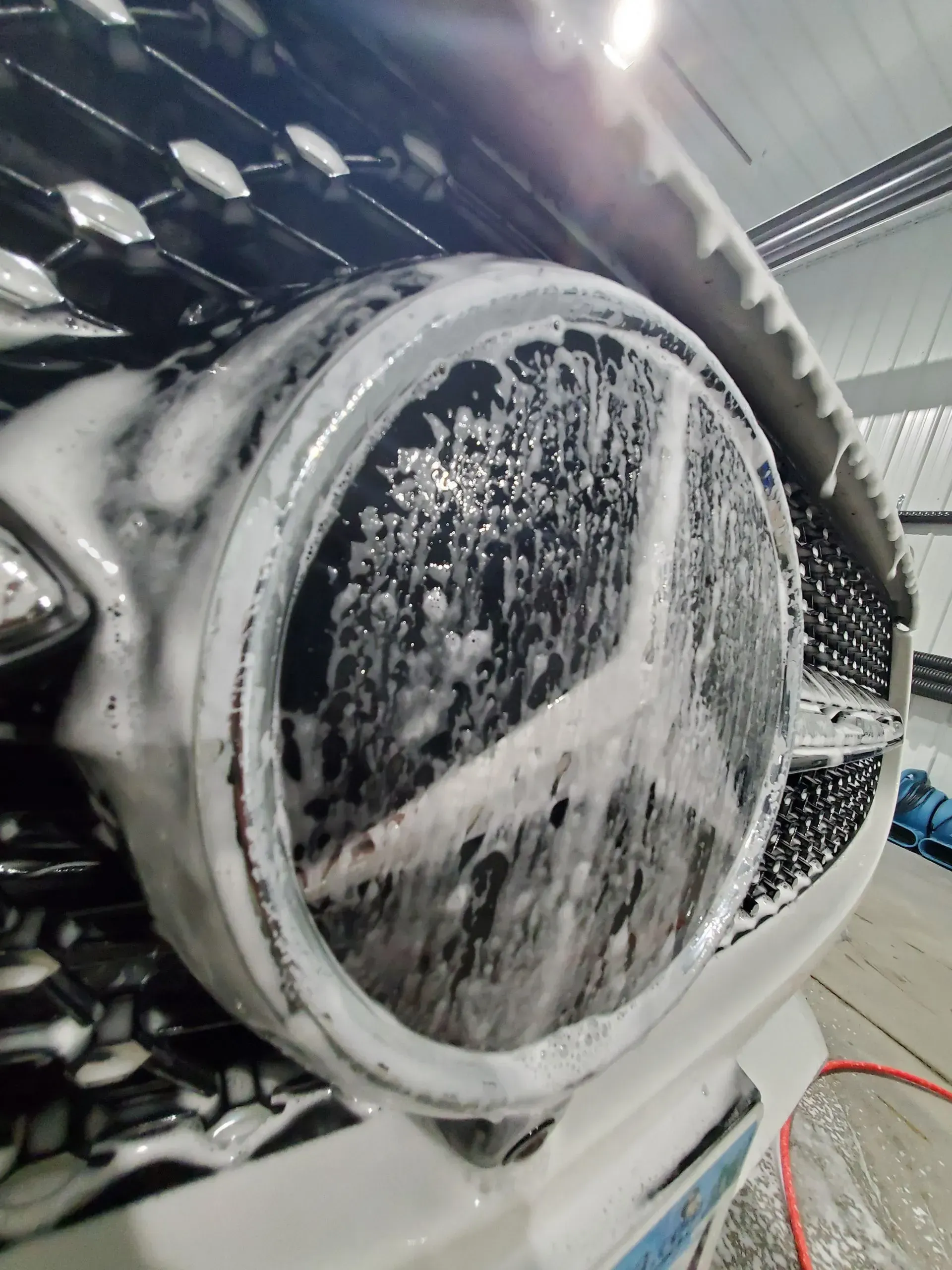 The front of a mercedes benz is being cleaned with soap and water.