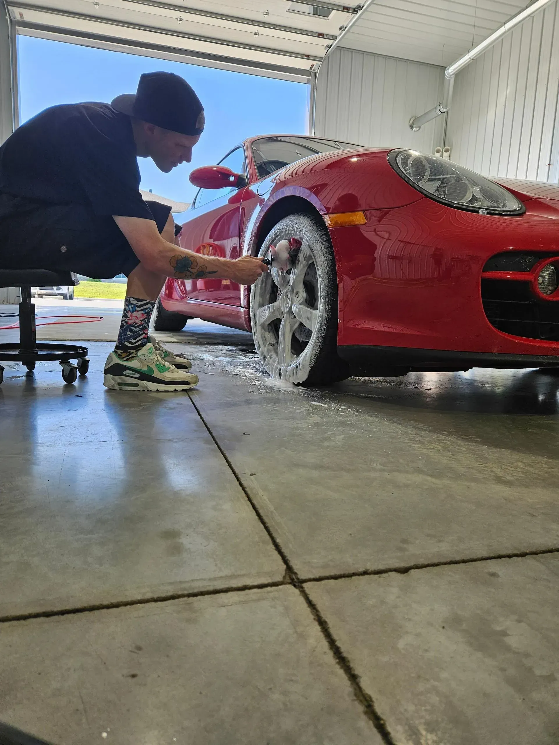 A man is washing a red sports car in a garage.