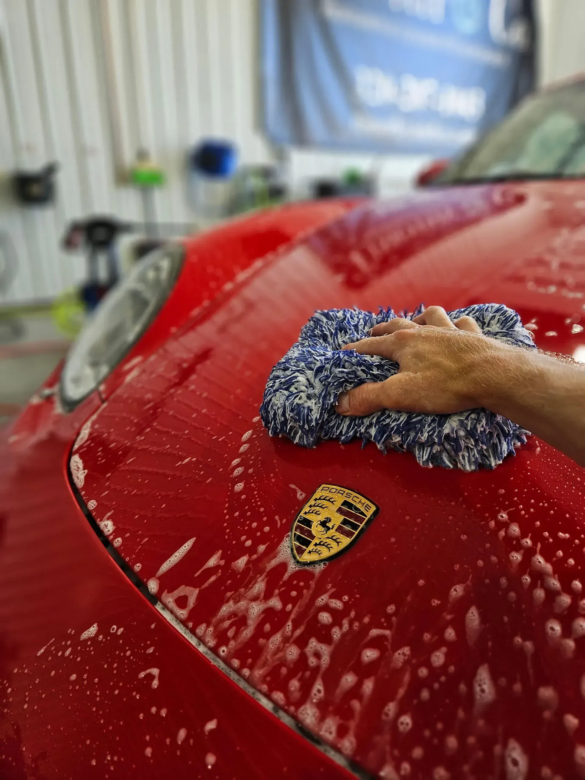 A person is washing a red porsche with a blue cloth