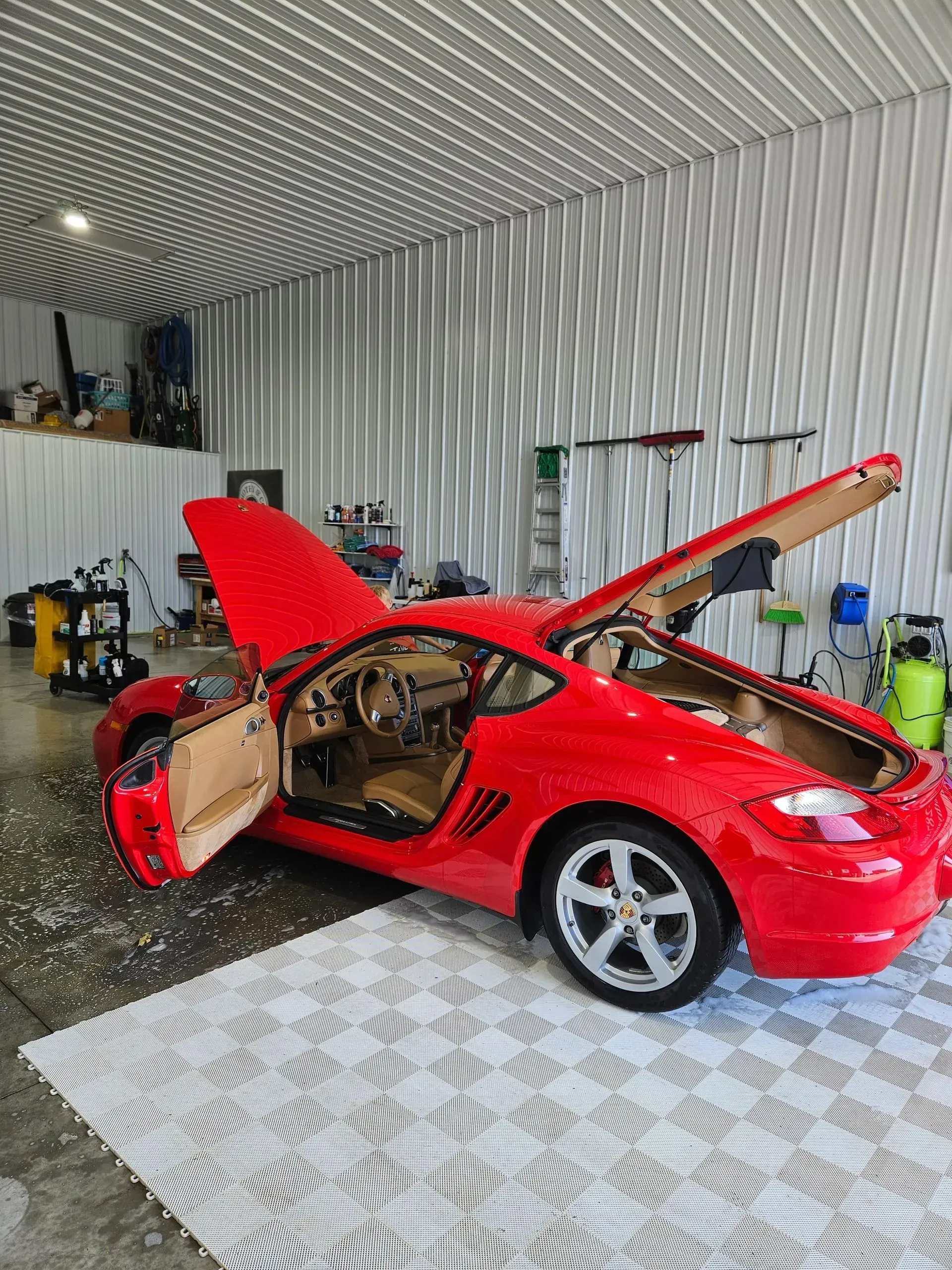 A red sports car is parked in a garage with its hood up.