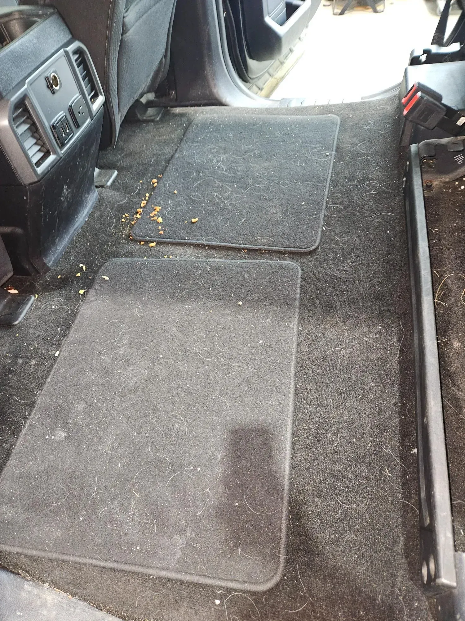 A dirty carpeted floor of a car with a few pieces of carpet on it.