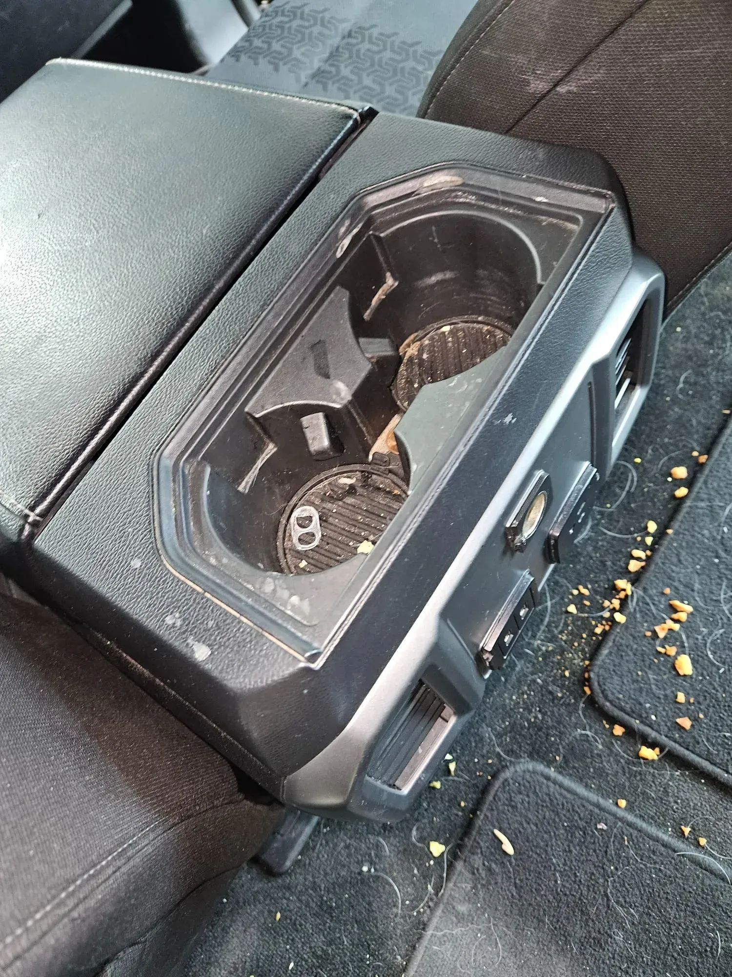 A dirty cup holder in the back seat of a car.
