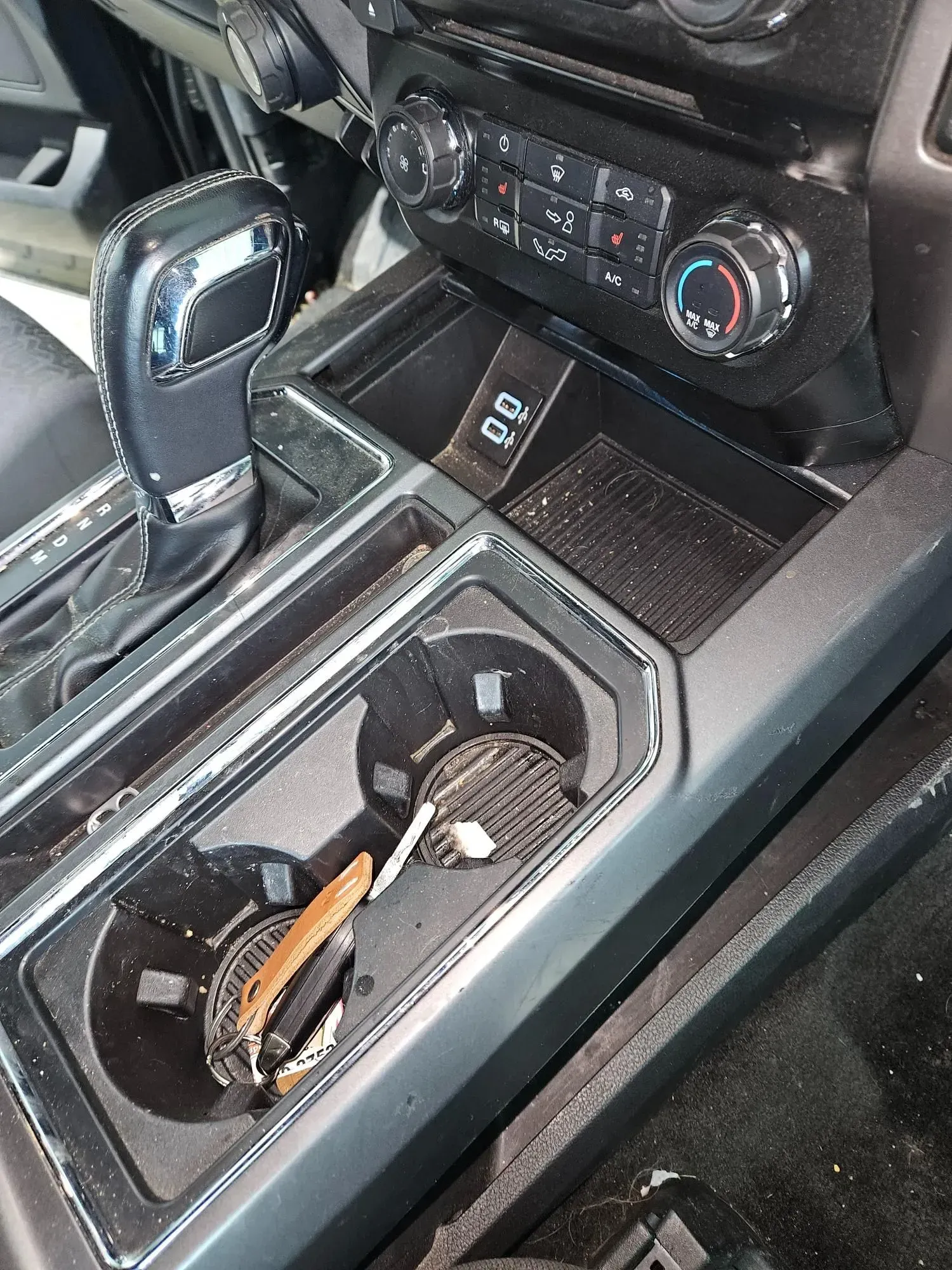 A close up of a car console with a cup holder and a remote control.