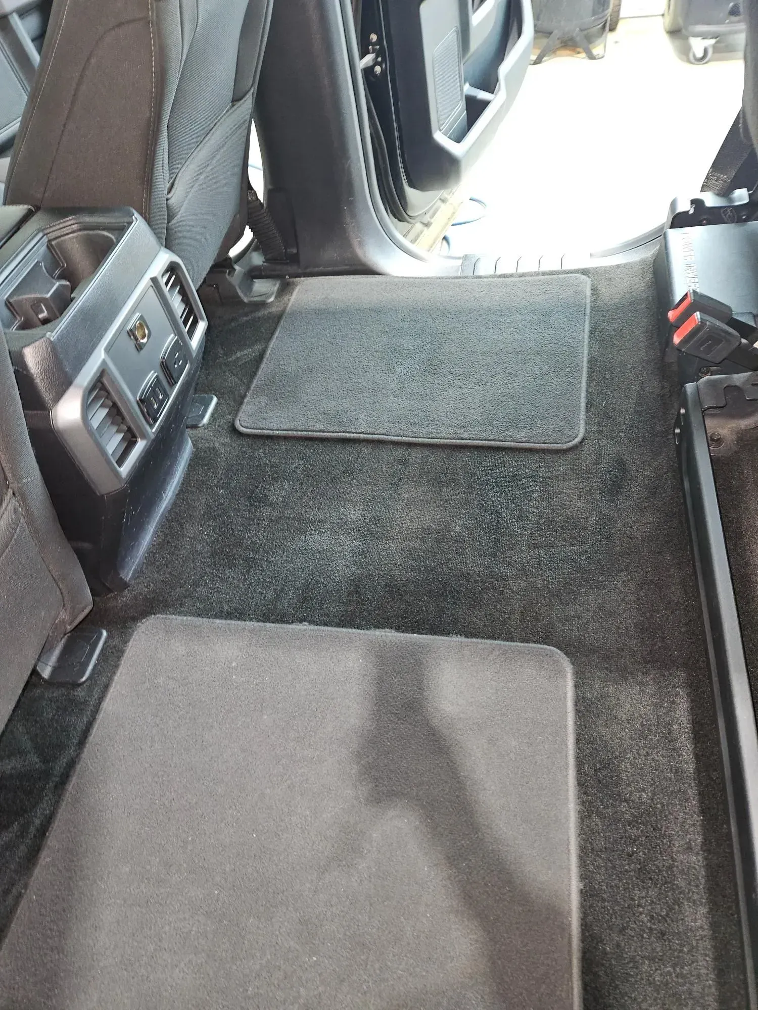 The back seat of a car with a carpeted floor.