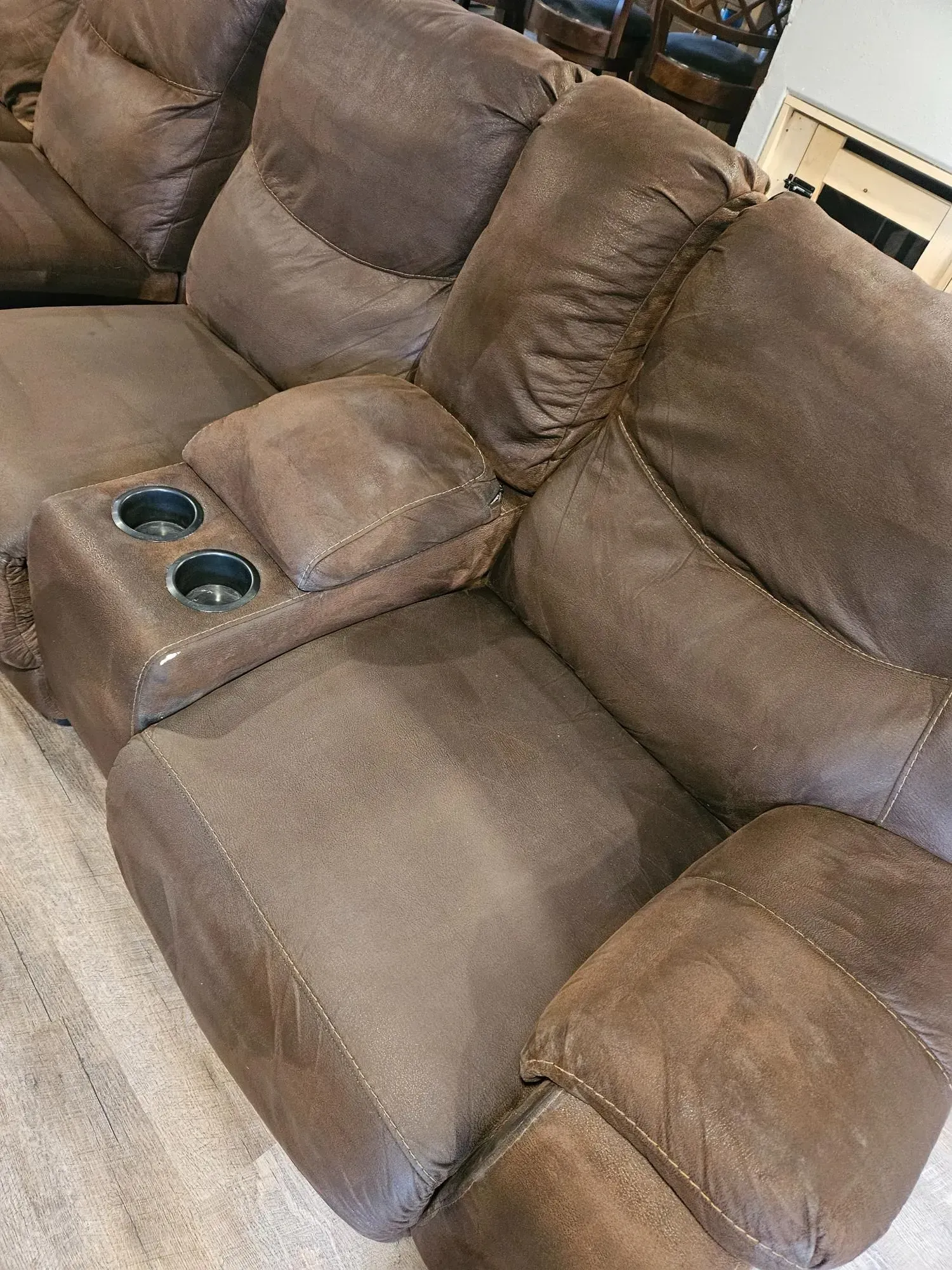 A brown recliner couch with two cup holders on the arm rests in a living room.