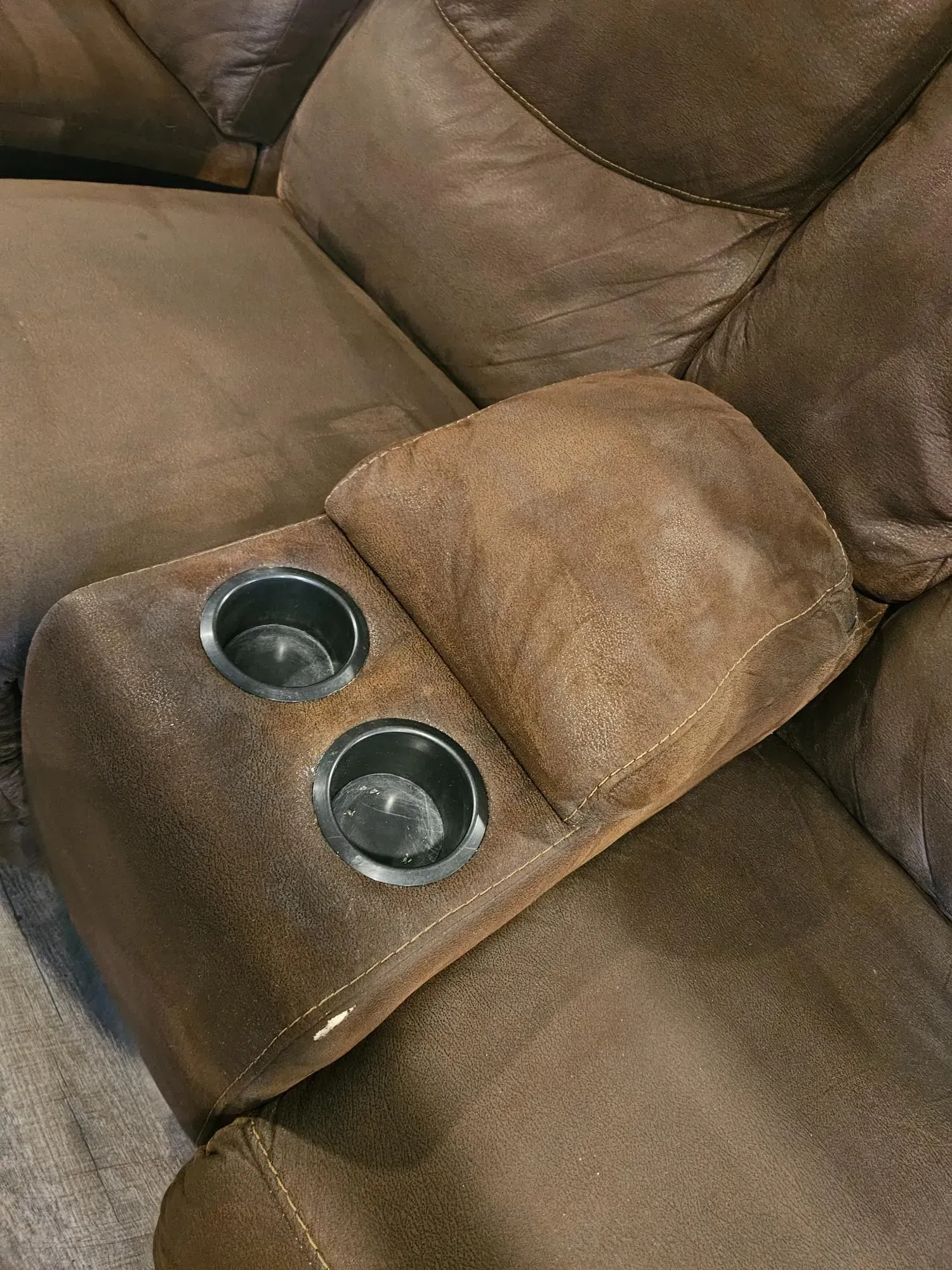 A brown leather recliner with two cup holders on the arm rests.