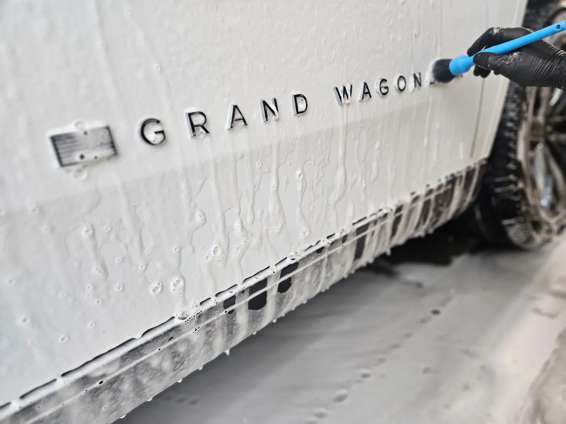 A person is washing a white grand wagon with a hose.