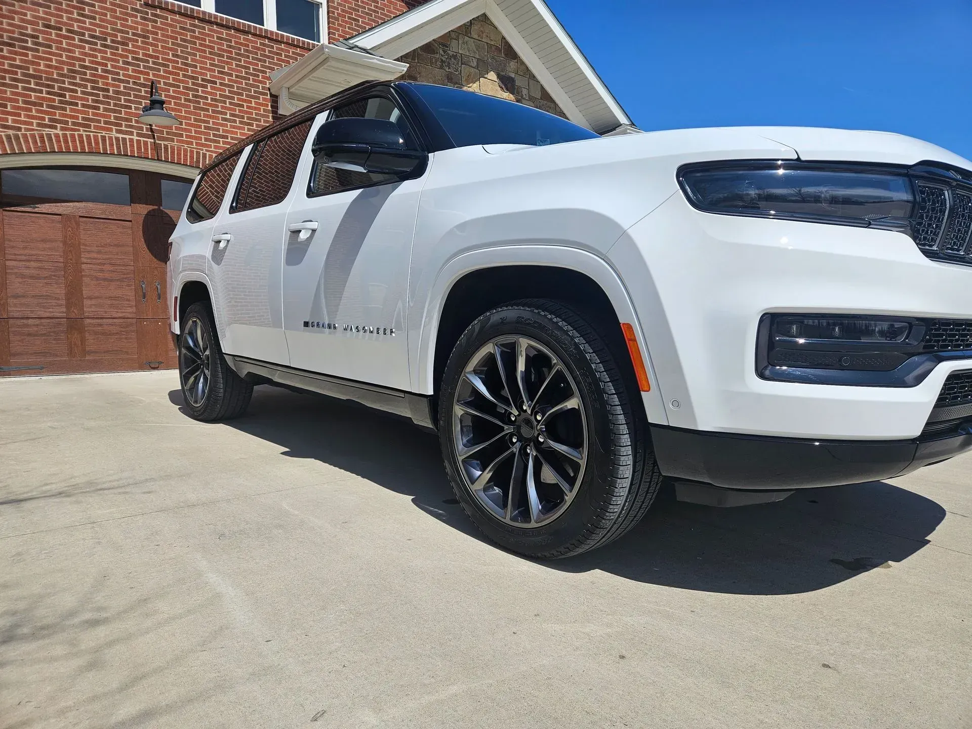A white suv is parked in a driveway in front of a brick house.