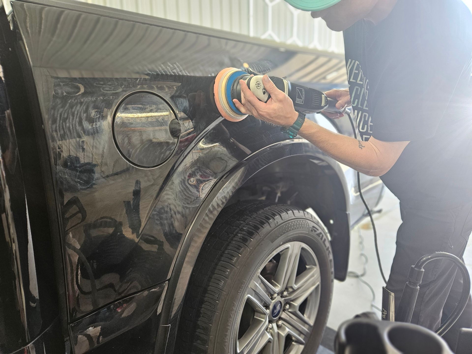 A person is polishing a black car with a machine.
