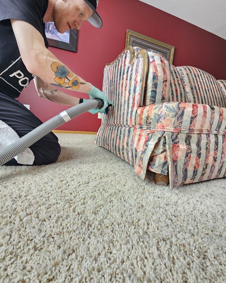 A man is cleaning a couch with a vacuum cleaner.