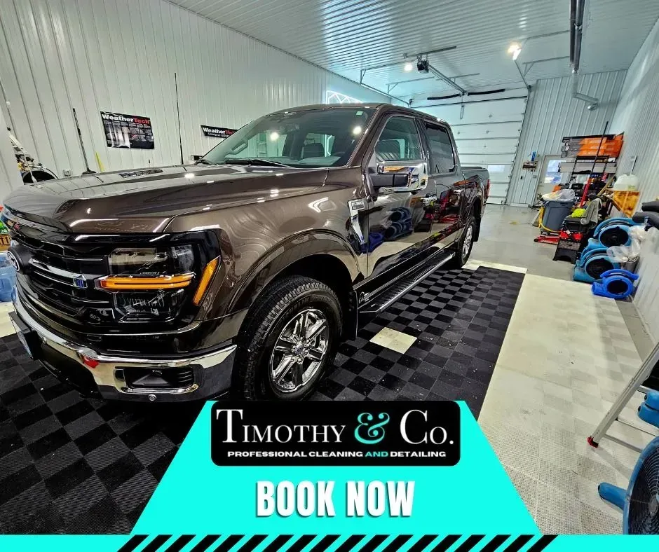 A truck is parked in a garage next to a sign that says `` book now ''.