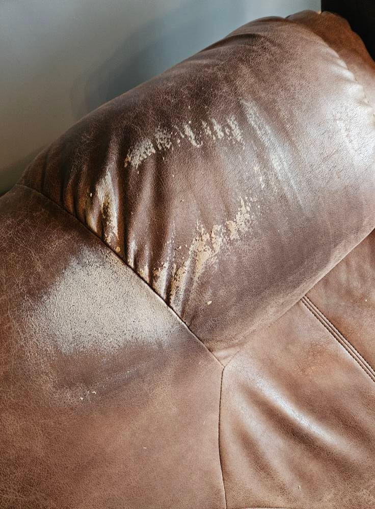 A close up of a brown leather couch with stains on it.