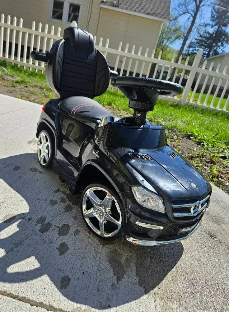 A black mercedes benz ride on car is parked on the side of the road.