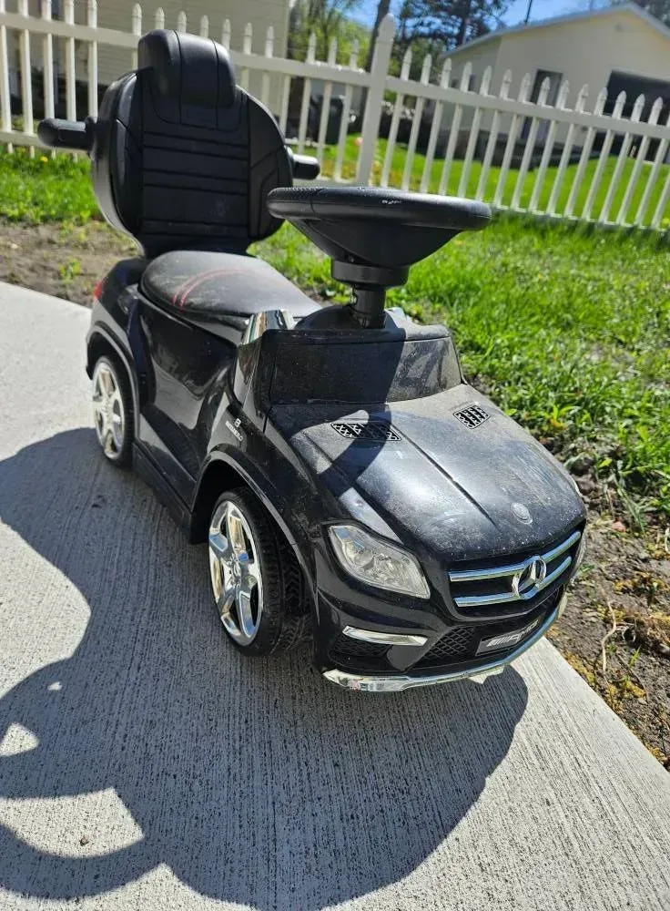 A black mercedes benz ride on car is parked on the side of the road.