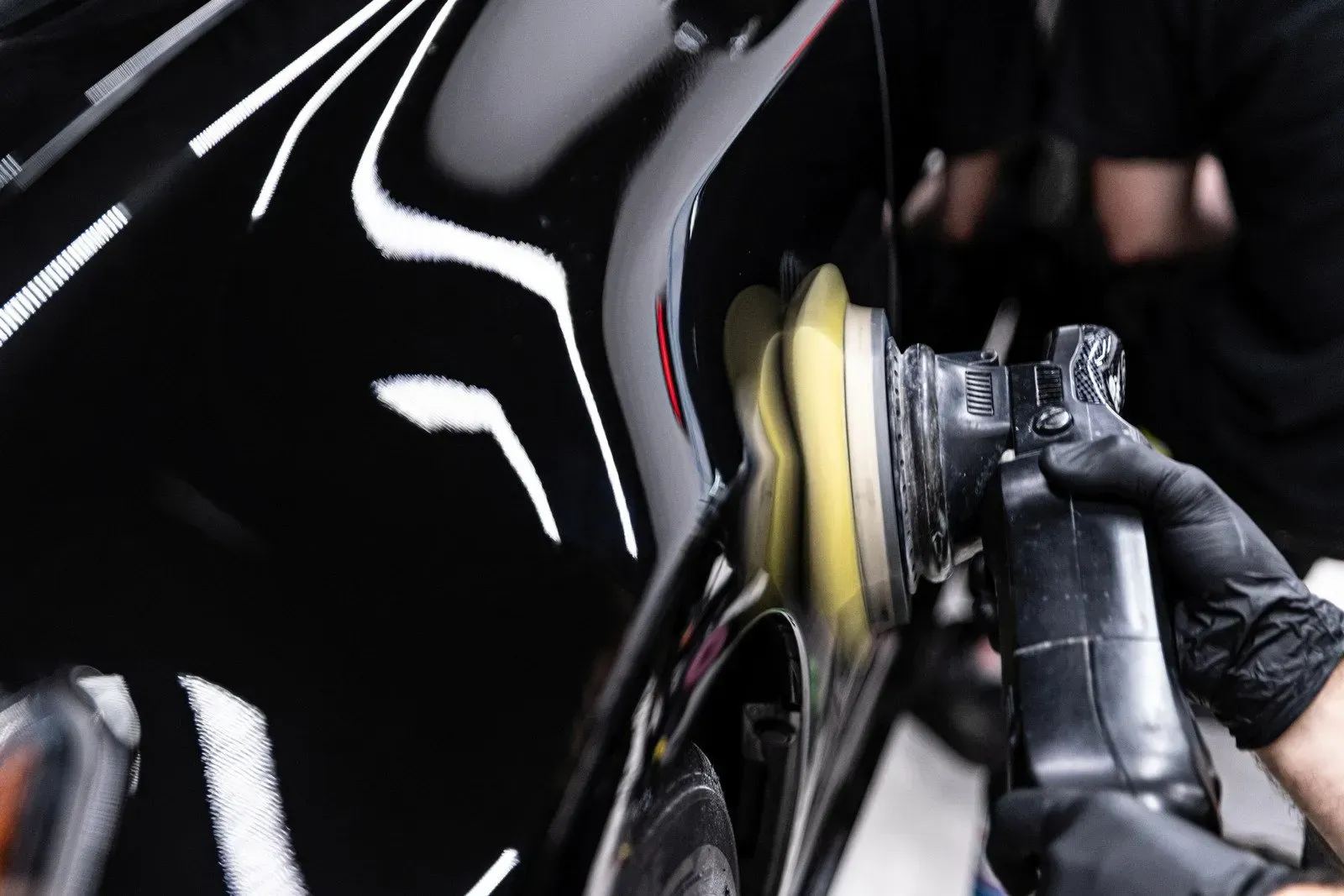 A person is polishing a black car with a machine.