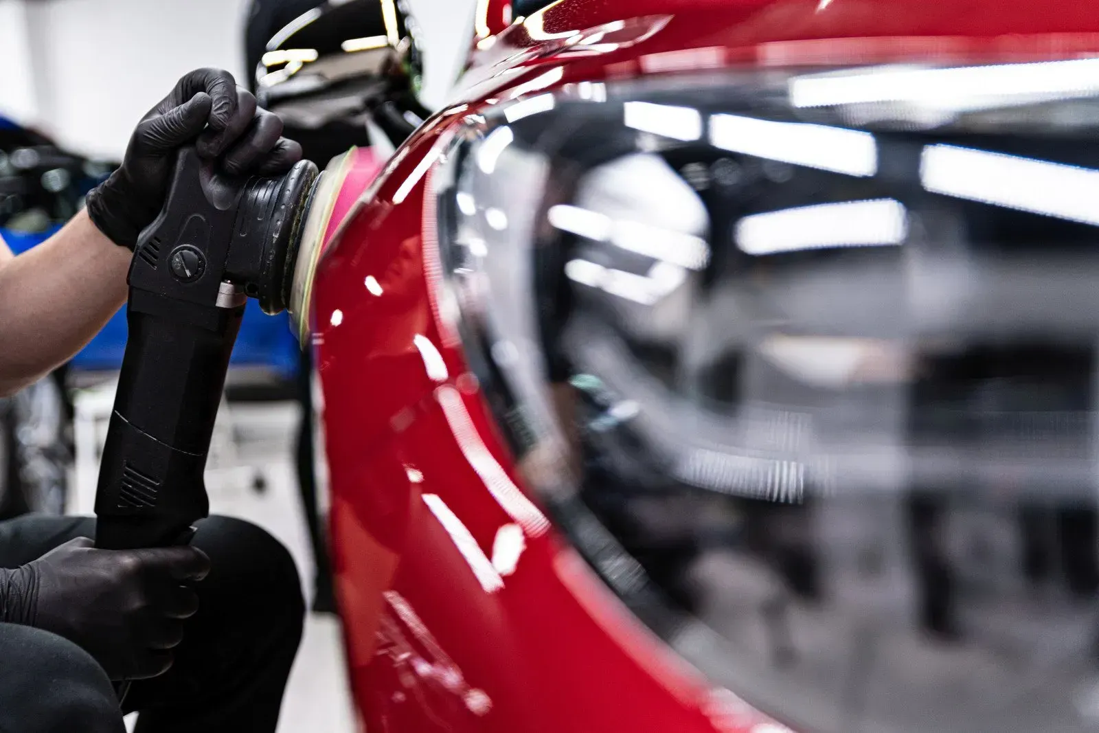 A man is polishing a red car in a garage.