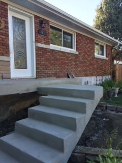 Une maison en briques avec des escaliers en béton menant à la porte d'entrée.