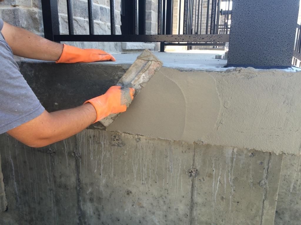 Un homme portant des gants orange enduit un mur avec une truelle.