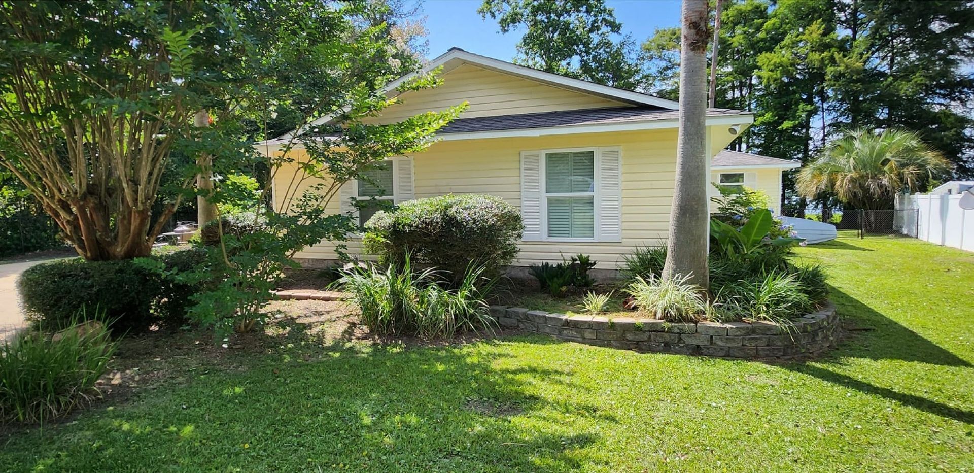 Yellow house with white trim, surrounded by green trees and grass, on a sunny day.
