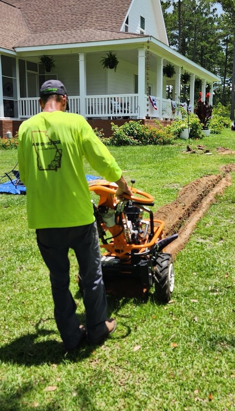 Man using a trenching machine in a grassy yard near a white house with a porch.