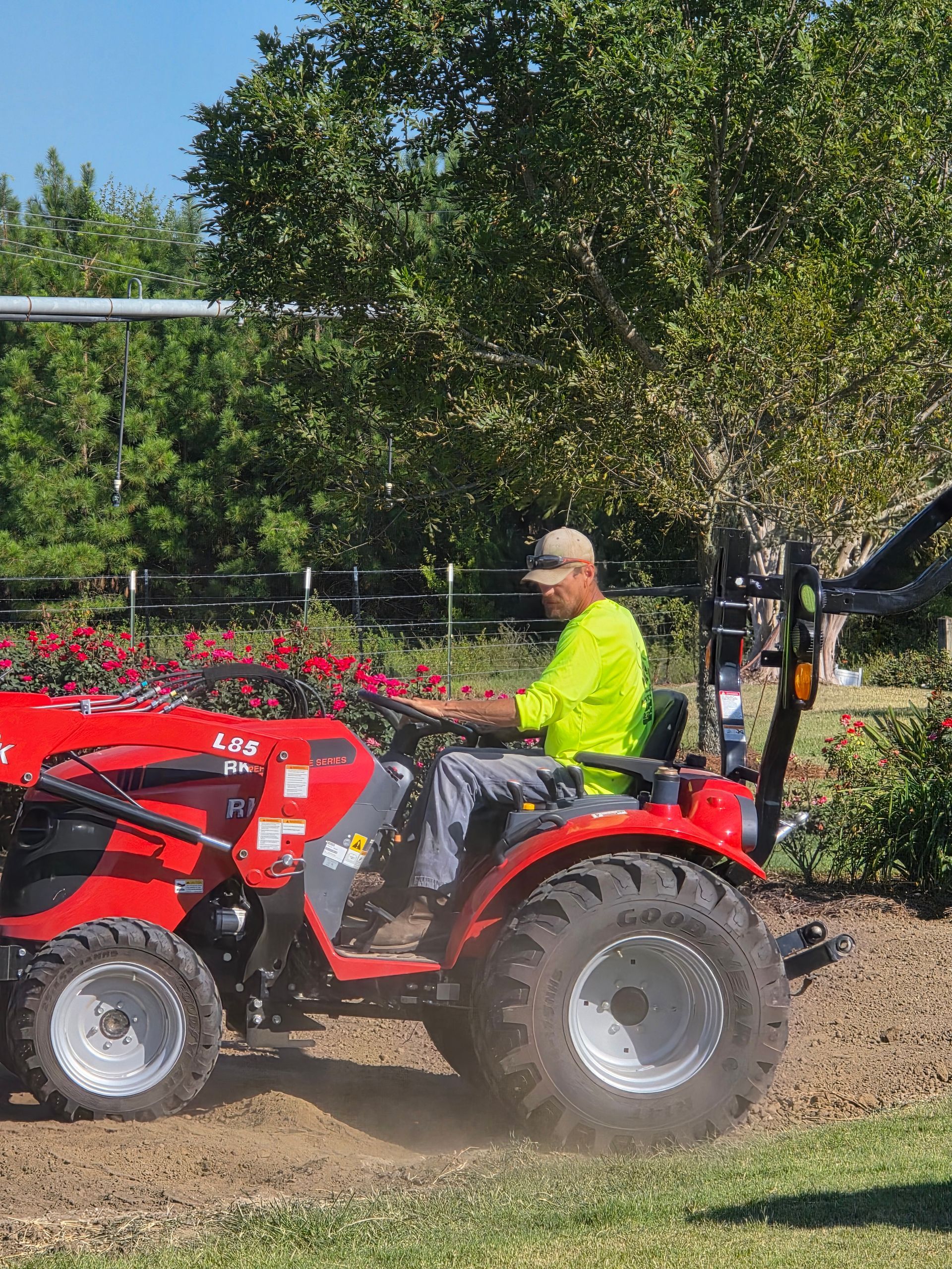 Man operating a red tractor, tilling soil in a garden on a sunny day.