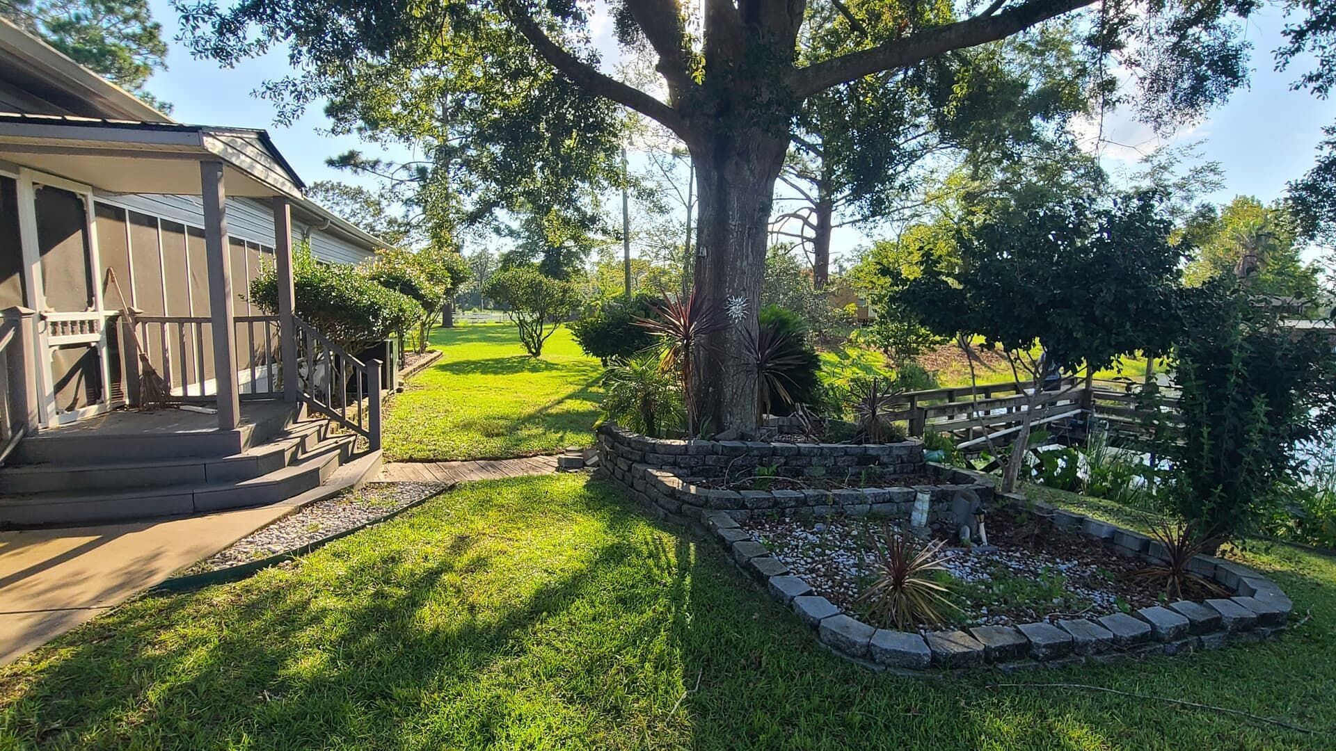 Lawn with screened porch and a tree surrounded by a rock garden near a body of water.