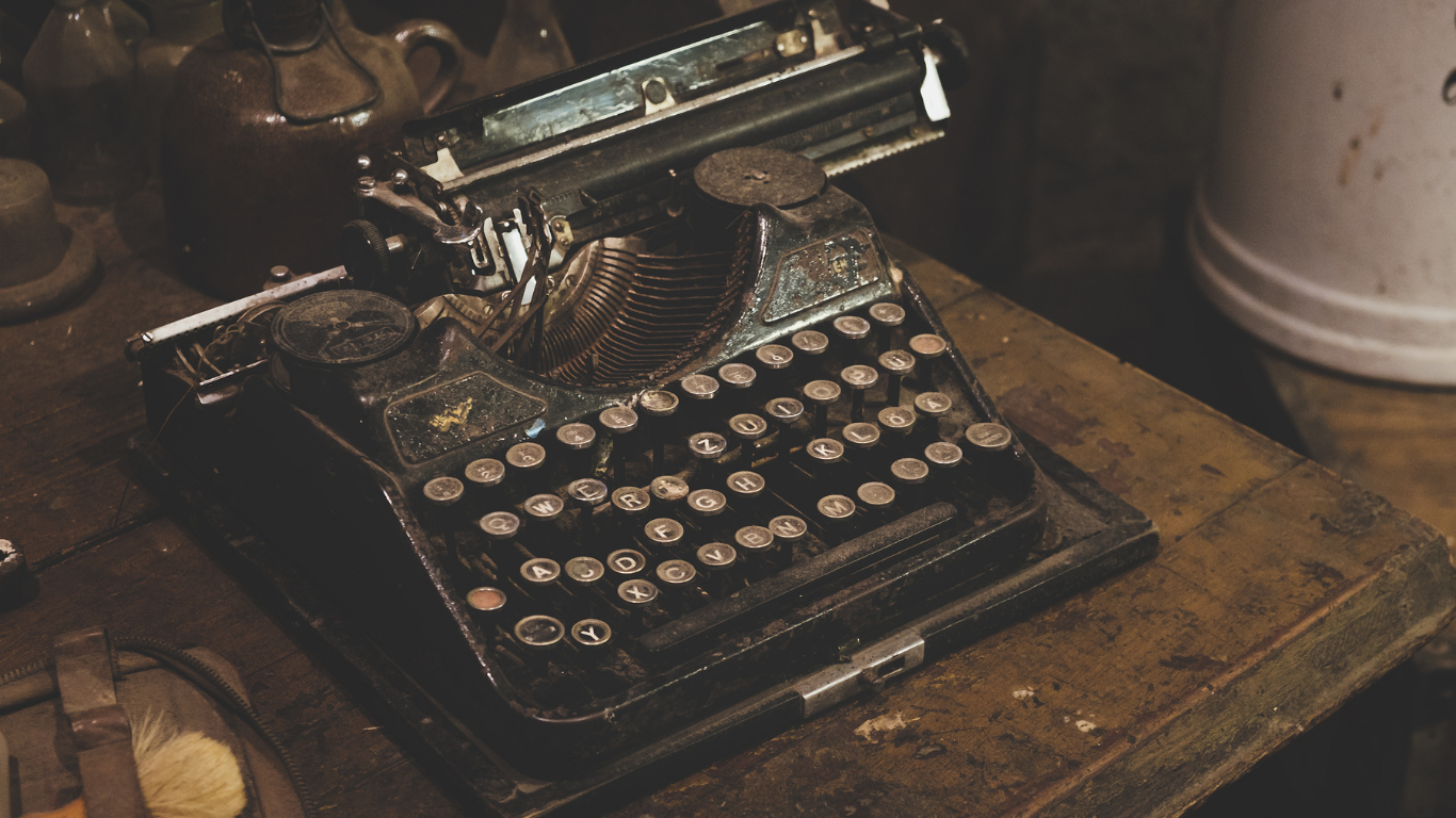 An old typewriter is sitting on a wooden table.