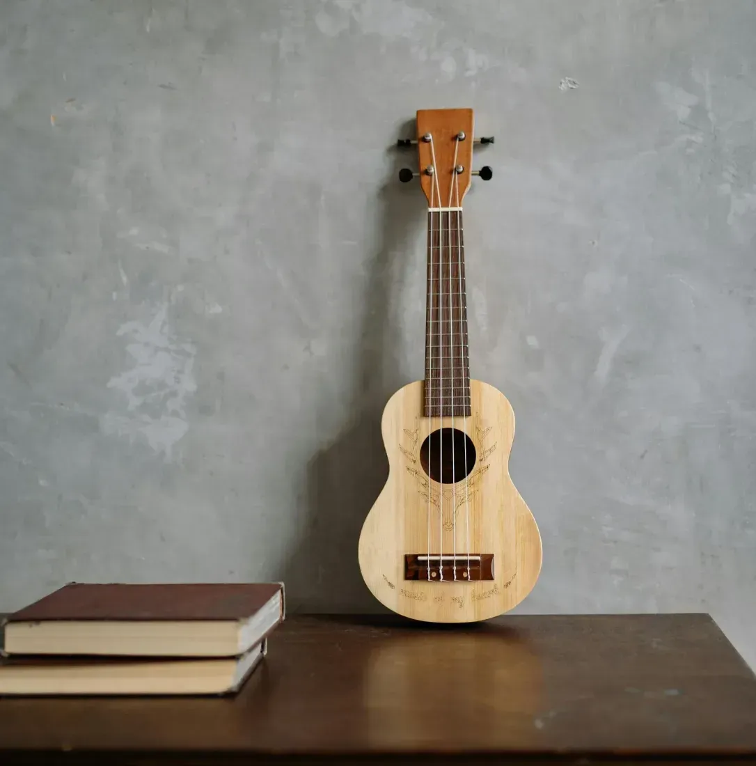 A ukulele is sitting on a wooden table next to two books.