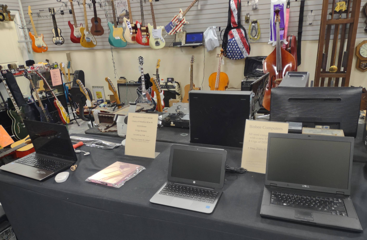 Several laptops are sitting on a table in front of a wall of guitars.