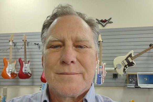 A man is taking a selfie in front of a wall of guitars.