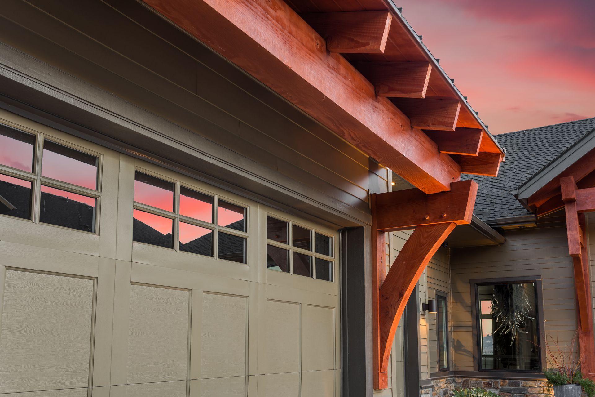 Close-up of a garage and house exterior with cream doors, wood beams, and a pink sunset sky