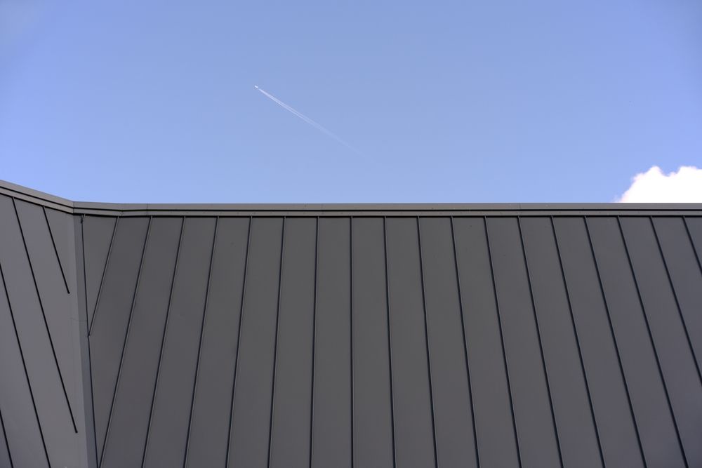A Plane is Flying in the Sky Above a Gray Roof — Apex Roofing Group in Grafton, NSW