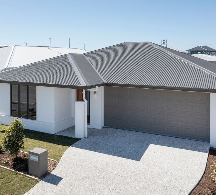 Contemporary single-storey home with a dark grey corrugated metal roof and matching garage door, featuring a white rendered facade and pebble driveway. — Apex Roofing Group in Byron Bay, NSW