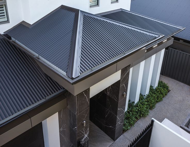 Modern dark grey corrugated metal roof with a hipped design, paired with sleek architectural elements including black marble pillars and clean white walls.— Apex Roofing Group in Yamba, NSW