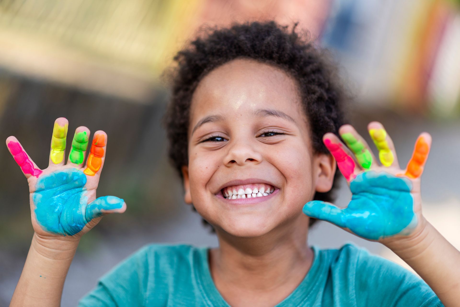 Smiling child with colorful painted hands held up against a blurred background