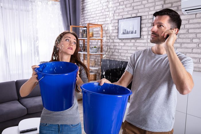 Paar steht im Wohnzimmer und fängt Wasser in Kübeln auf - Wasserschaden Notruf