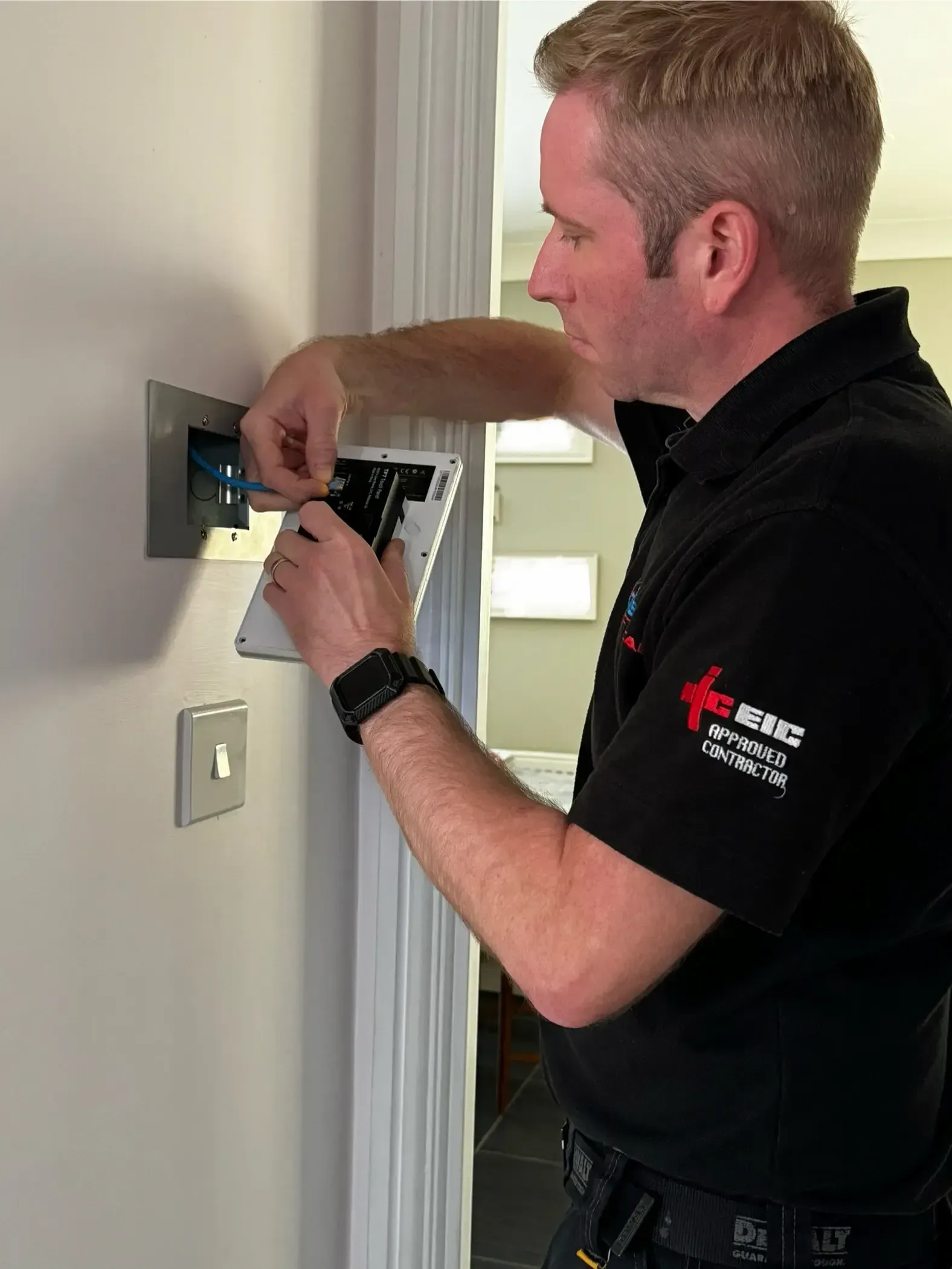 An electrician from AJOB Electrical Ltd is working on a smart home touchscreen control panel.