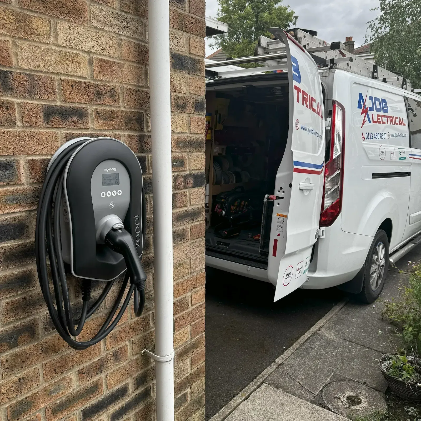 EV charger on brick wall with an electrician's van parked nearby.