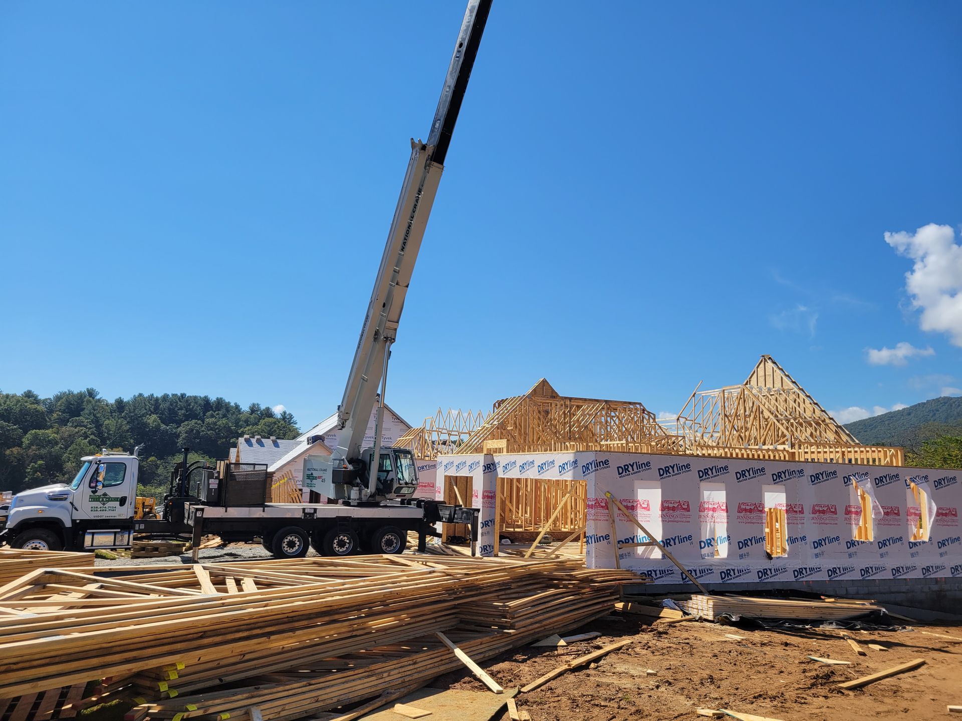 A crane lifting a wall panel onto a new home construction site on a sunny day.